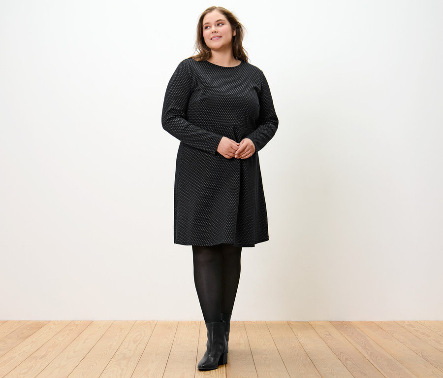 Žena stojí a má na sobě žakárové šaty se třpytivým efektem.