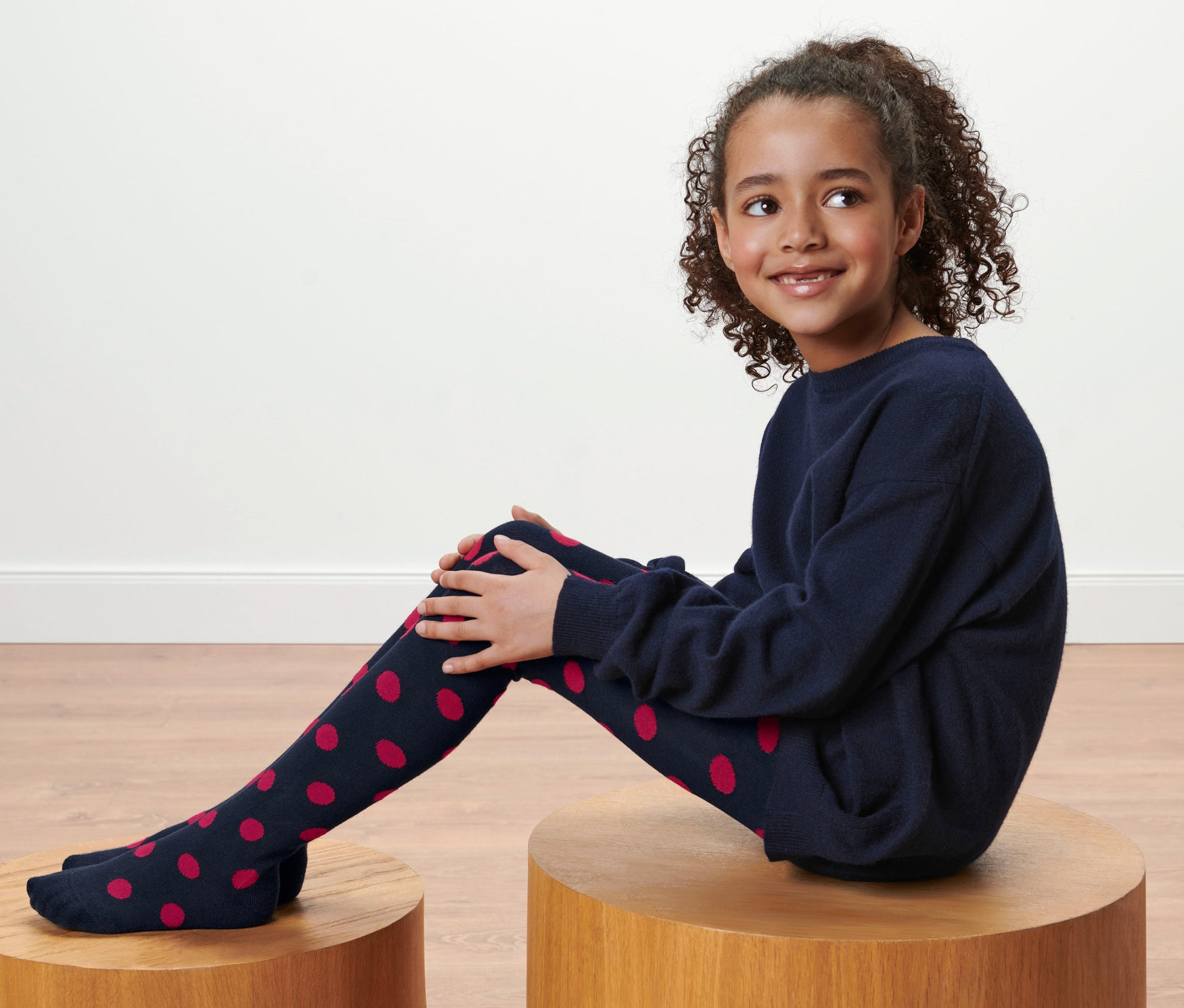 Dívka sedí na dřevěném stolku a má na sobě tmavě modré punčocháče s červenými puntíky, 2 ks.