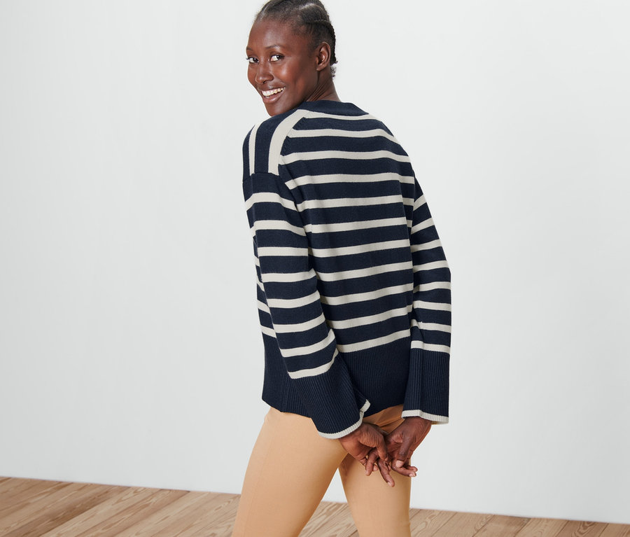 Žena se ohlíží přes rameno a má na sobě pruhovaný kardigan.