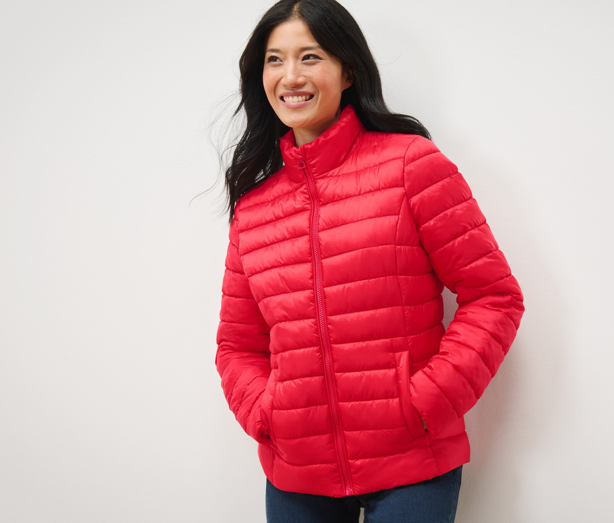 Žena usmívá se a pózuje v červené prošívané bundě.