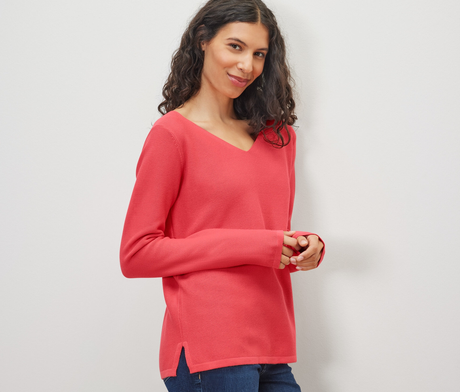 Žena má na sobě korálový pletený svetr a džíny.