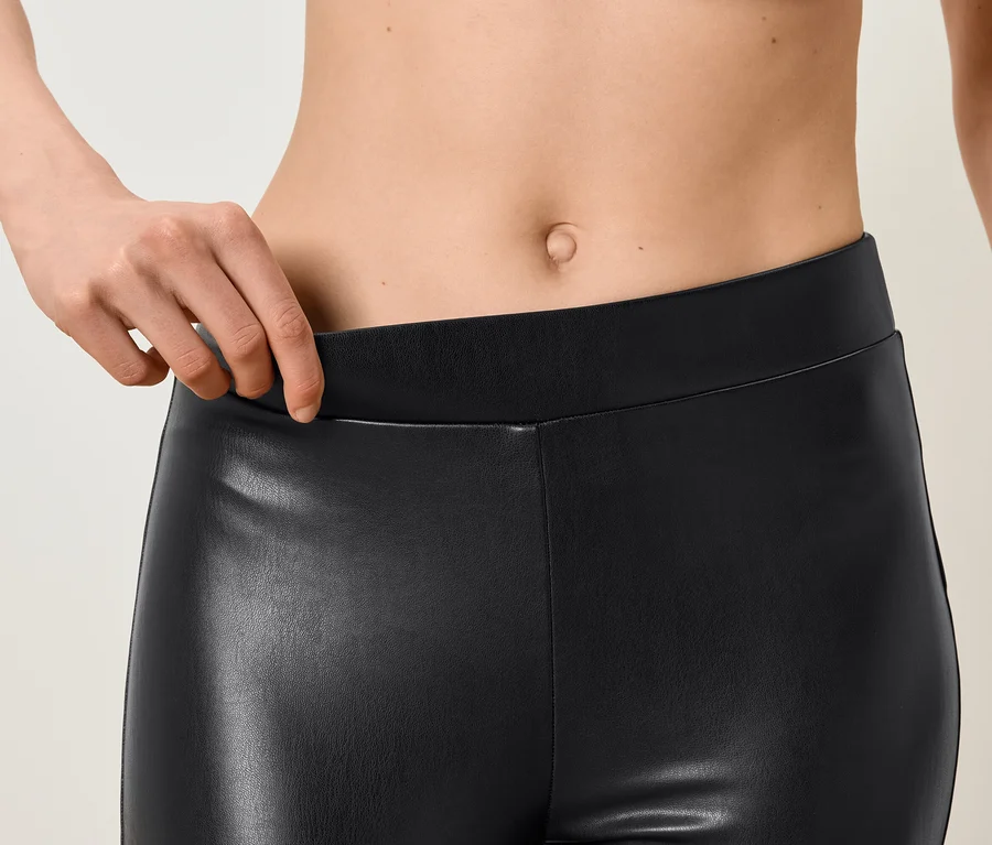 Detailní záběr na ženu držící pas černých koženkových legín.