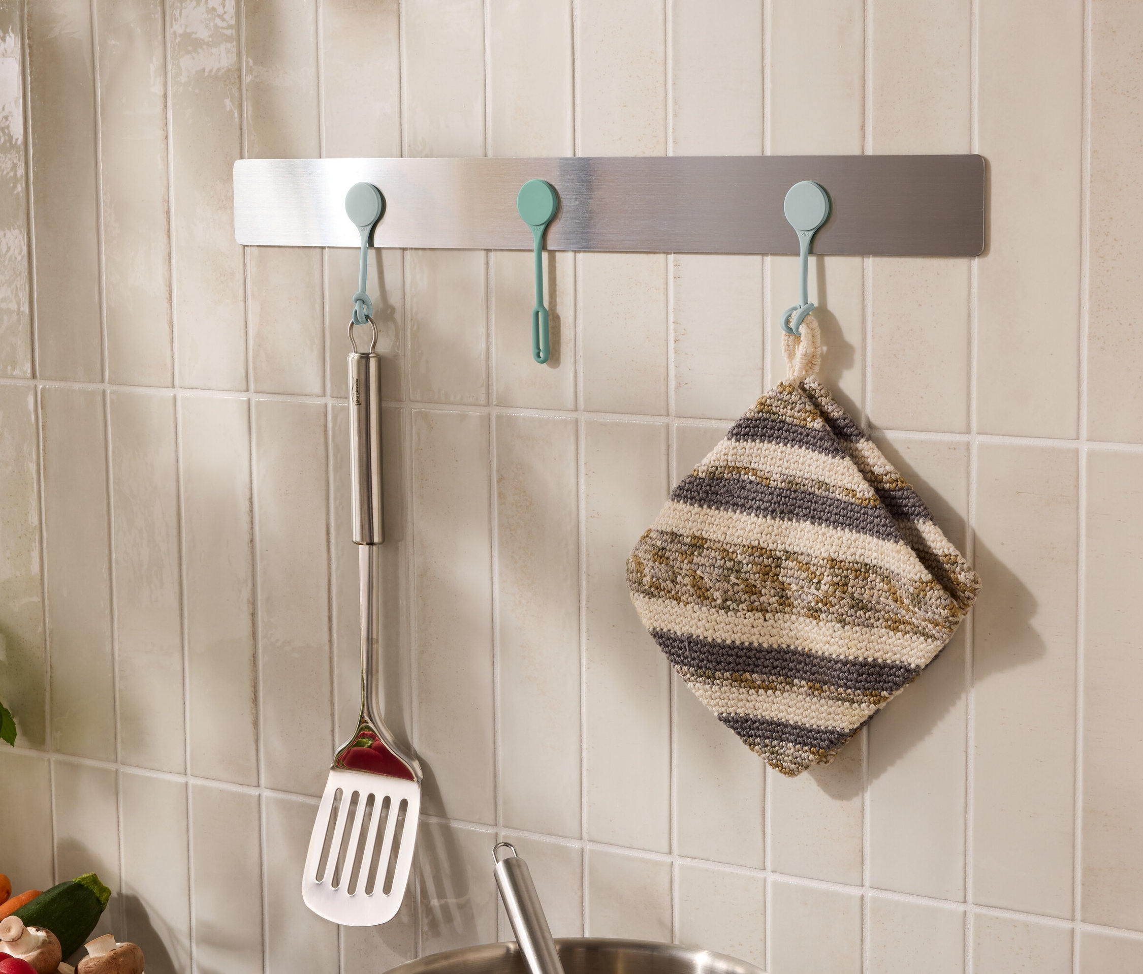 Na zdi visí na háčcích kuchyňské náčiní, například obracečka a utěrka.