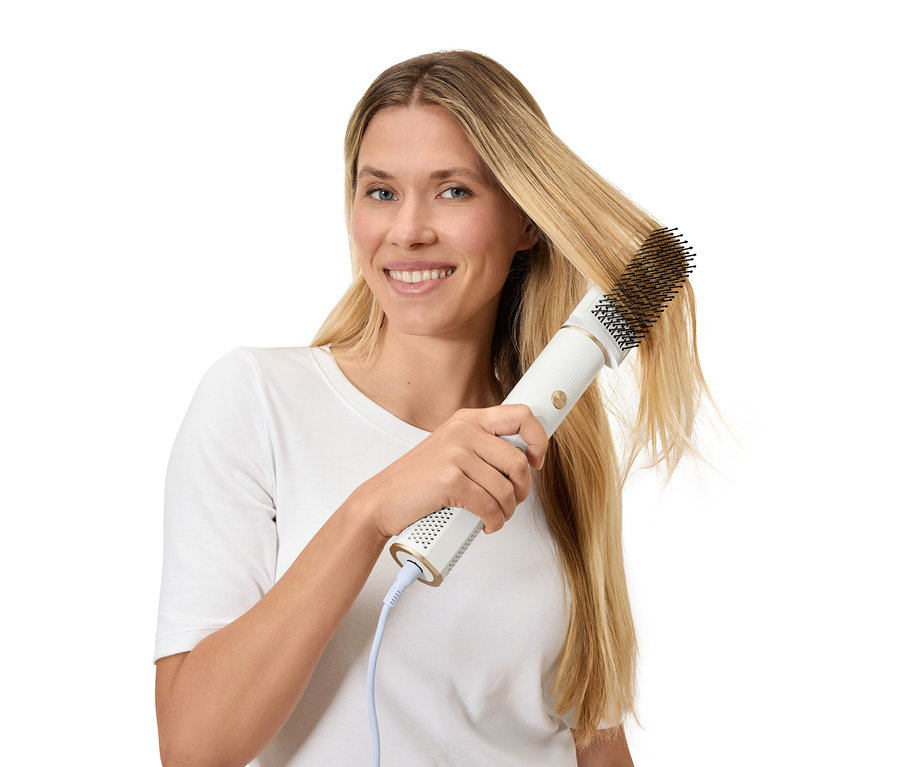 Žena si upravuje blond vlasy kulmofénem.