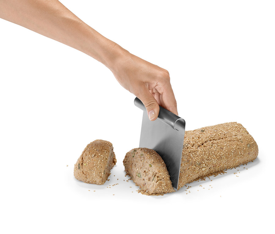 Ruka krájí bochník chleba sypaný semínky pomocí kovového nože.