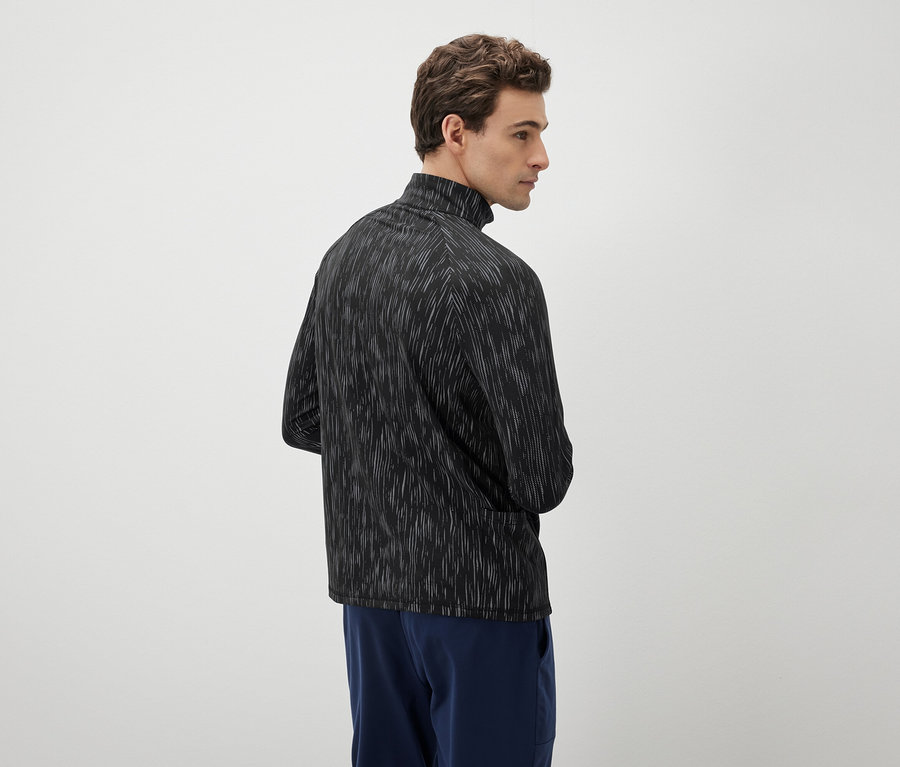 Muž se dívá doleva a má na sobě černo-bílý top a modré kalhoty.