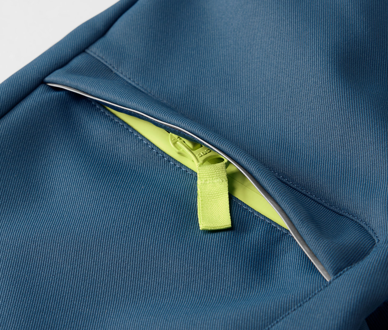 Detail dětských softshellových kalhot s neonově zeleným zipem.