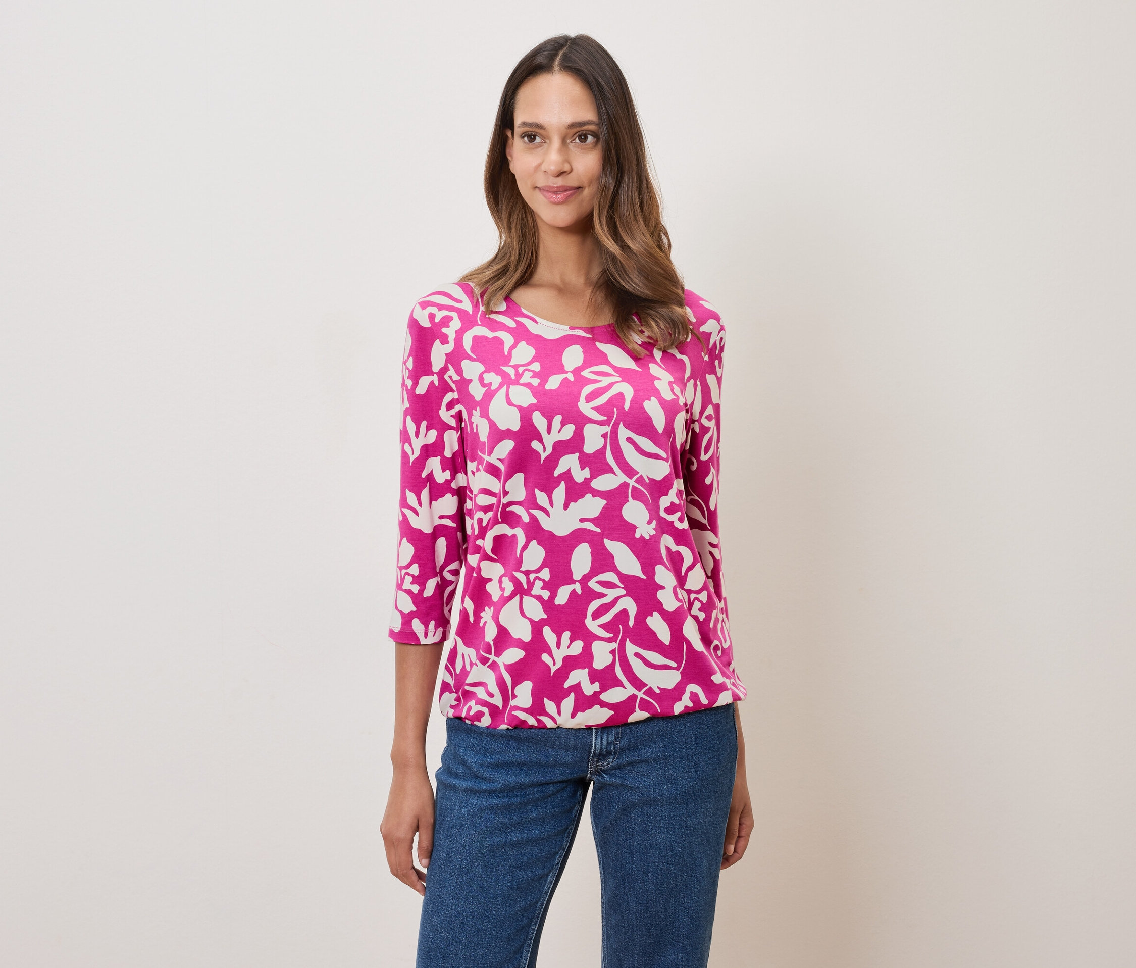 Žena má na sobě růžovou halenku s květinovým vzorem a džíny.