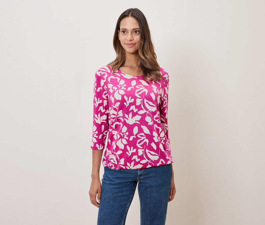 Žena má na sobě růžovou halenku s květinovým vzorem a džíny.