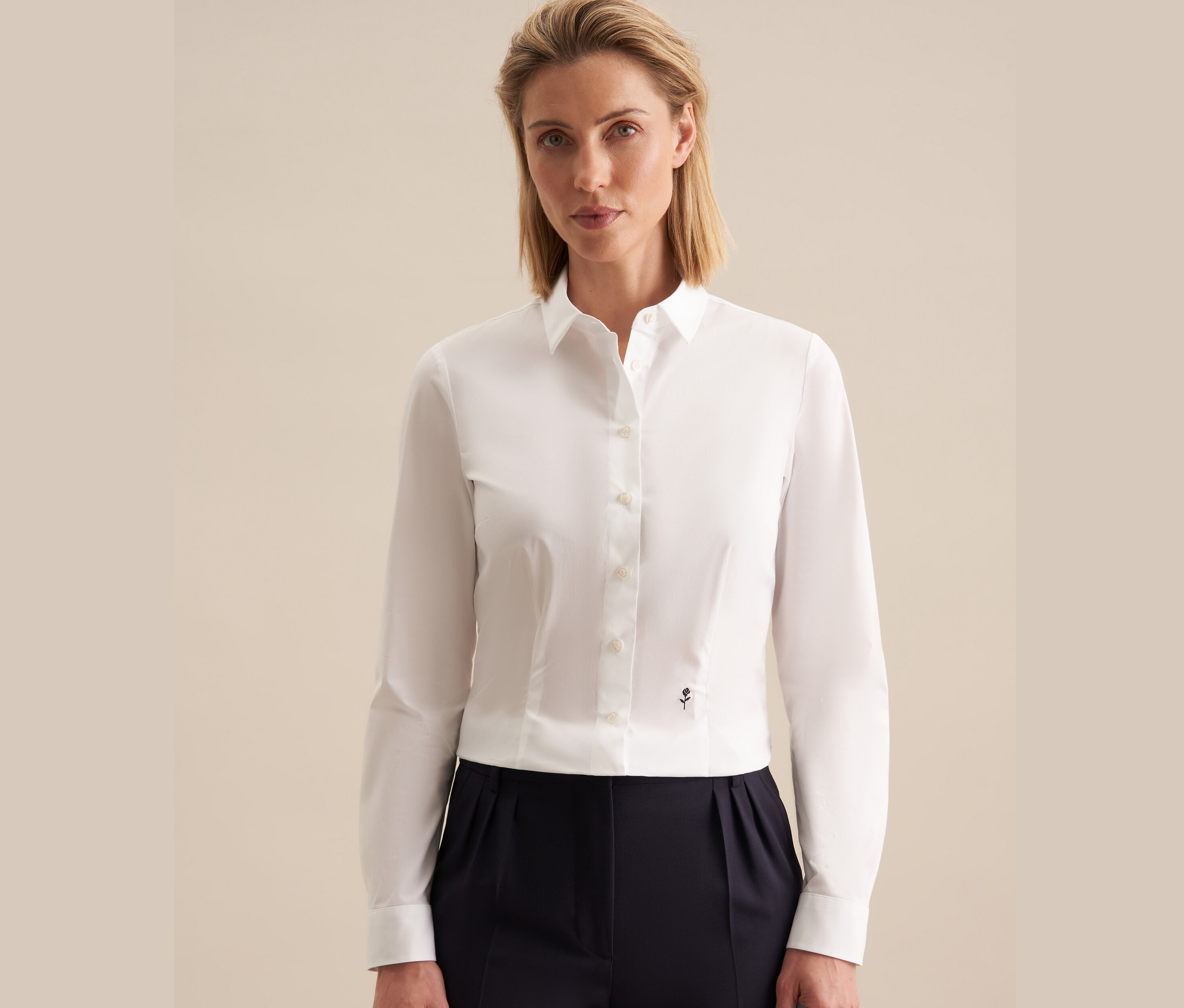 Žena má na sobě bílou halenku Seidensticker slim fit a tmavě modré kalhoty.