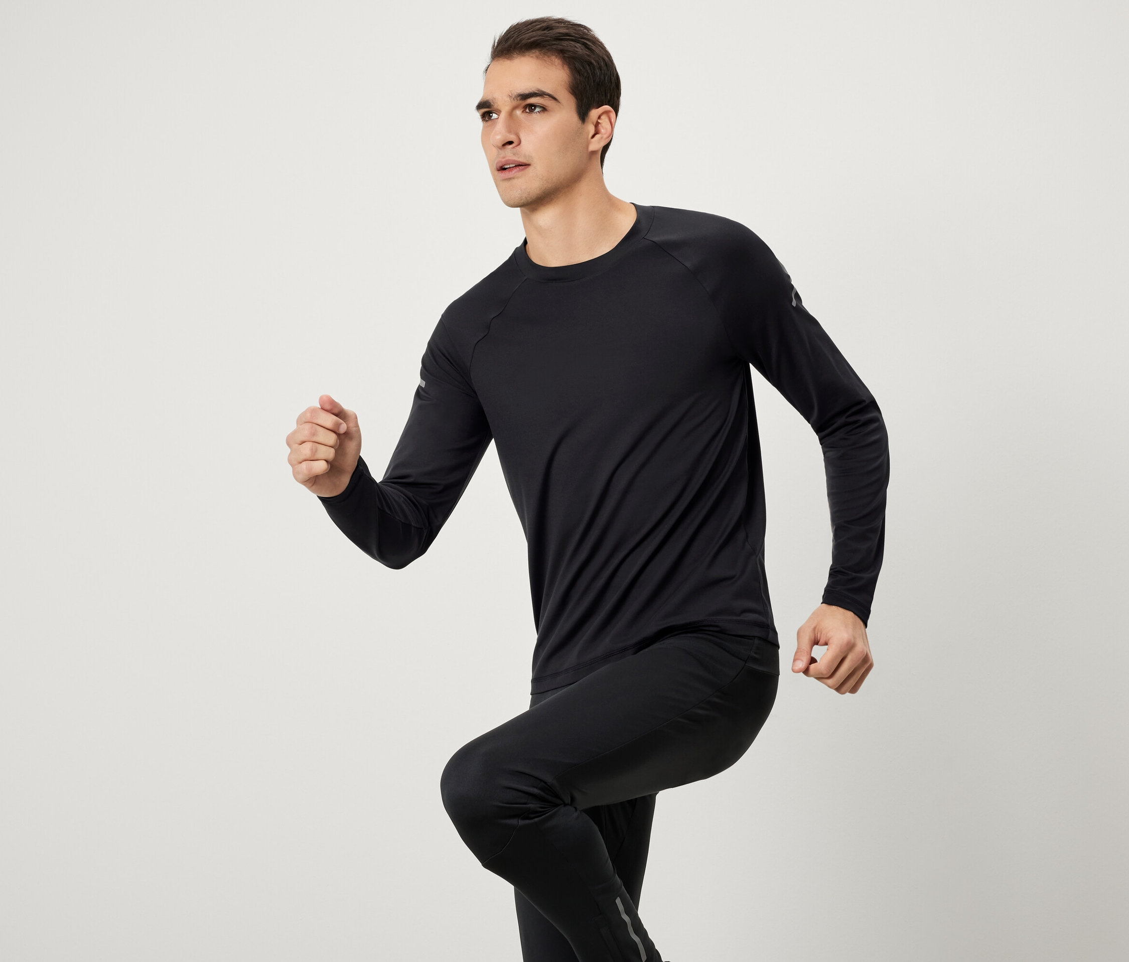 Muž v černém sportovním oblečení s dlouhým rukávem a kalhotami při běhu.