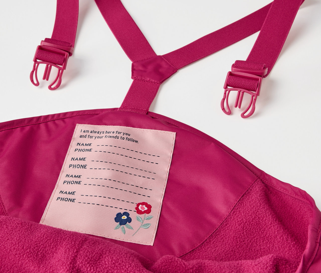 Detail dětských termo kalhot do deště bobulové barvy s laclem a štítkem na jméno.