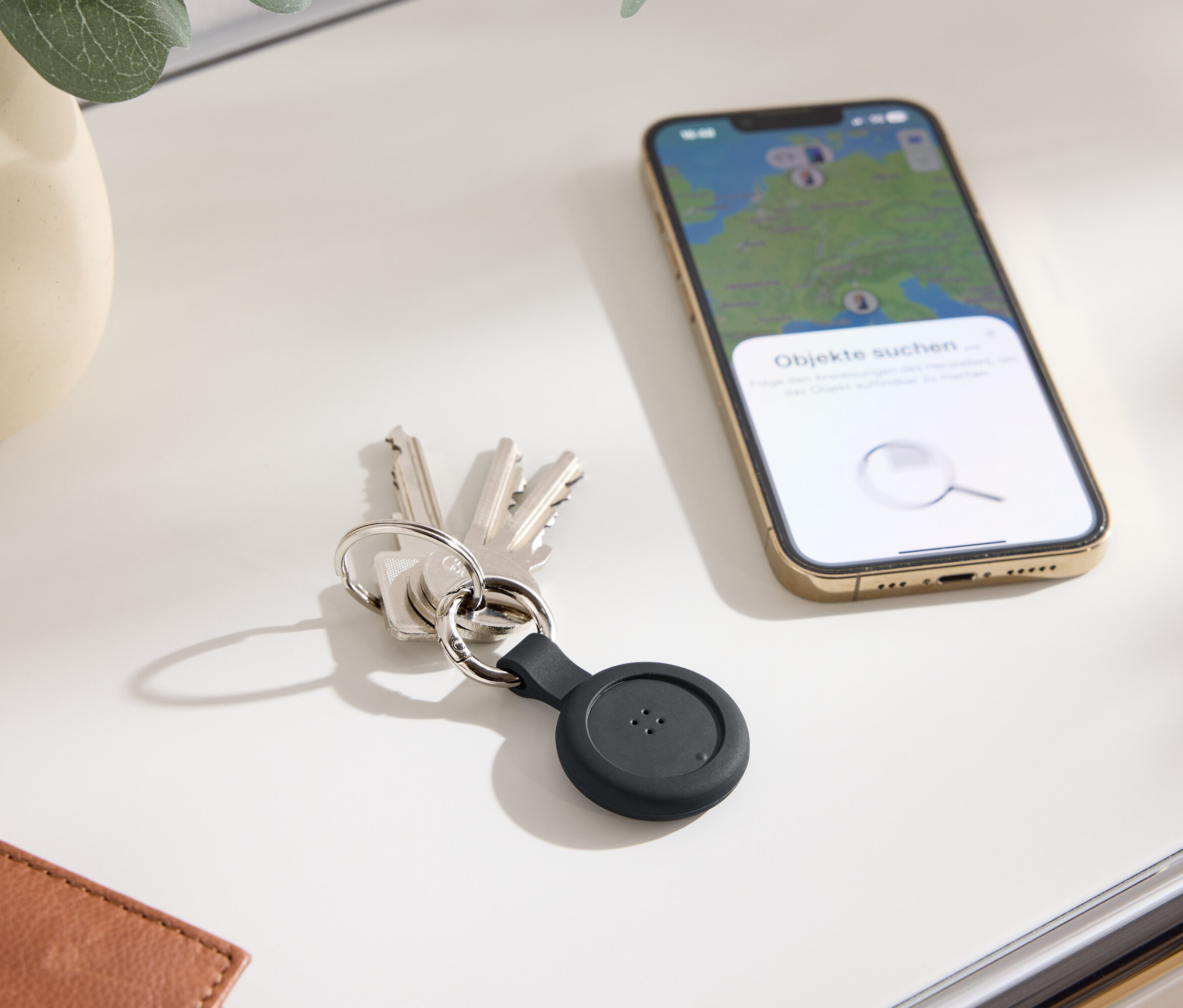 Klíče s černým lokátorem a mobilní telefon s mapou na displeji leží na stole.