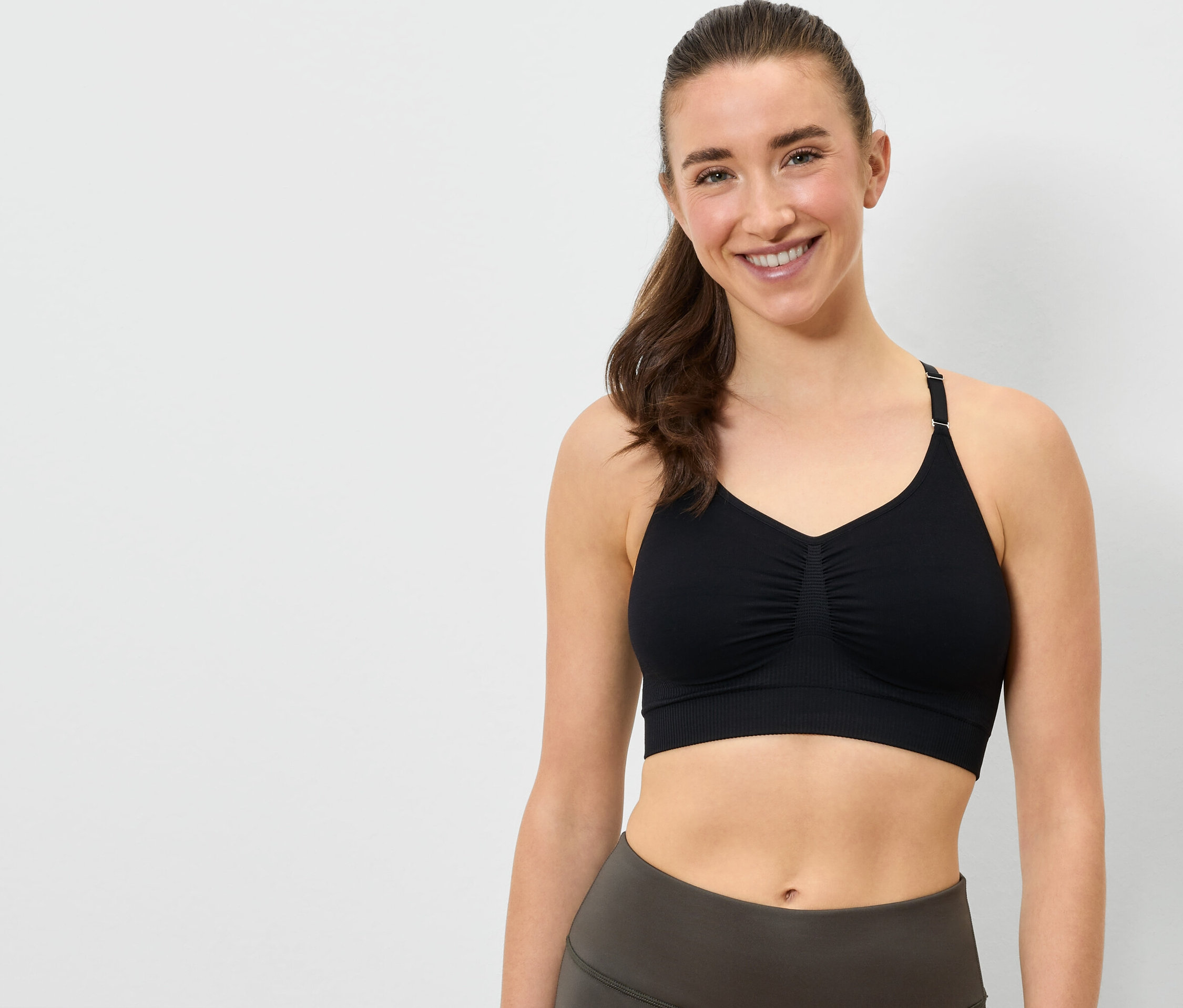Usmívající se žena má na sobě černou sportovní podprsenku a šedé legíny.