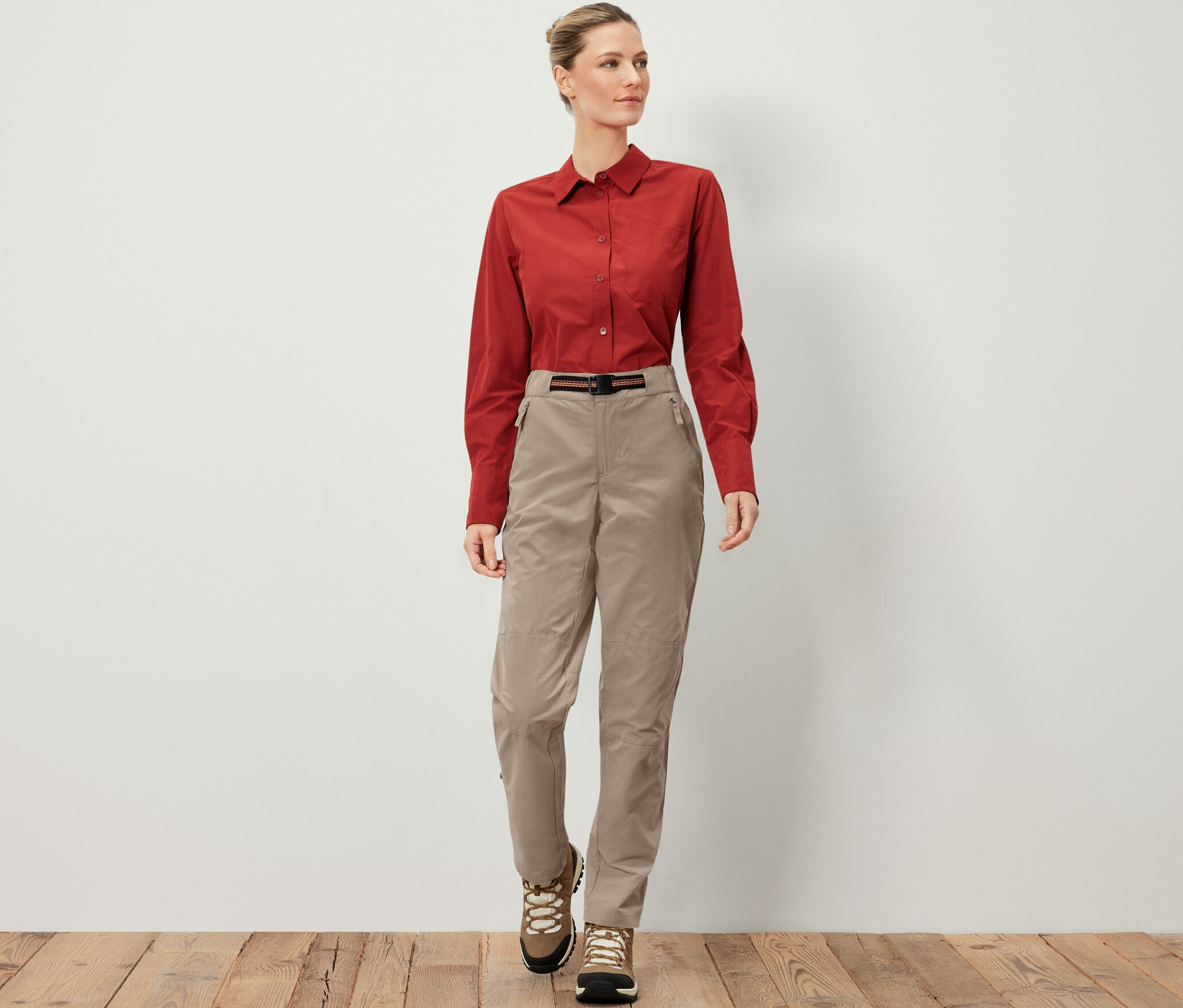 Žena má na sobě outdoorové kalhoty s ochranou proti komárům, hnědou košili a turistické boty.