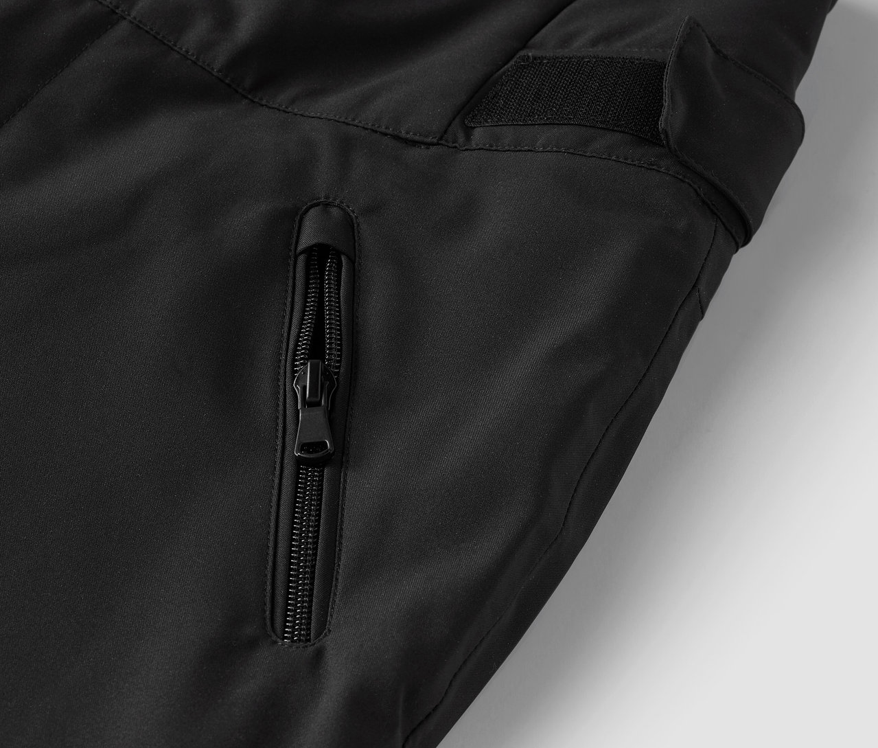 Detail černých kalhot s kapsou na zip.