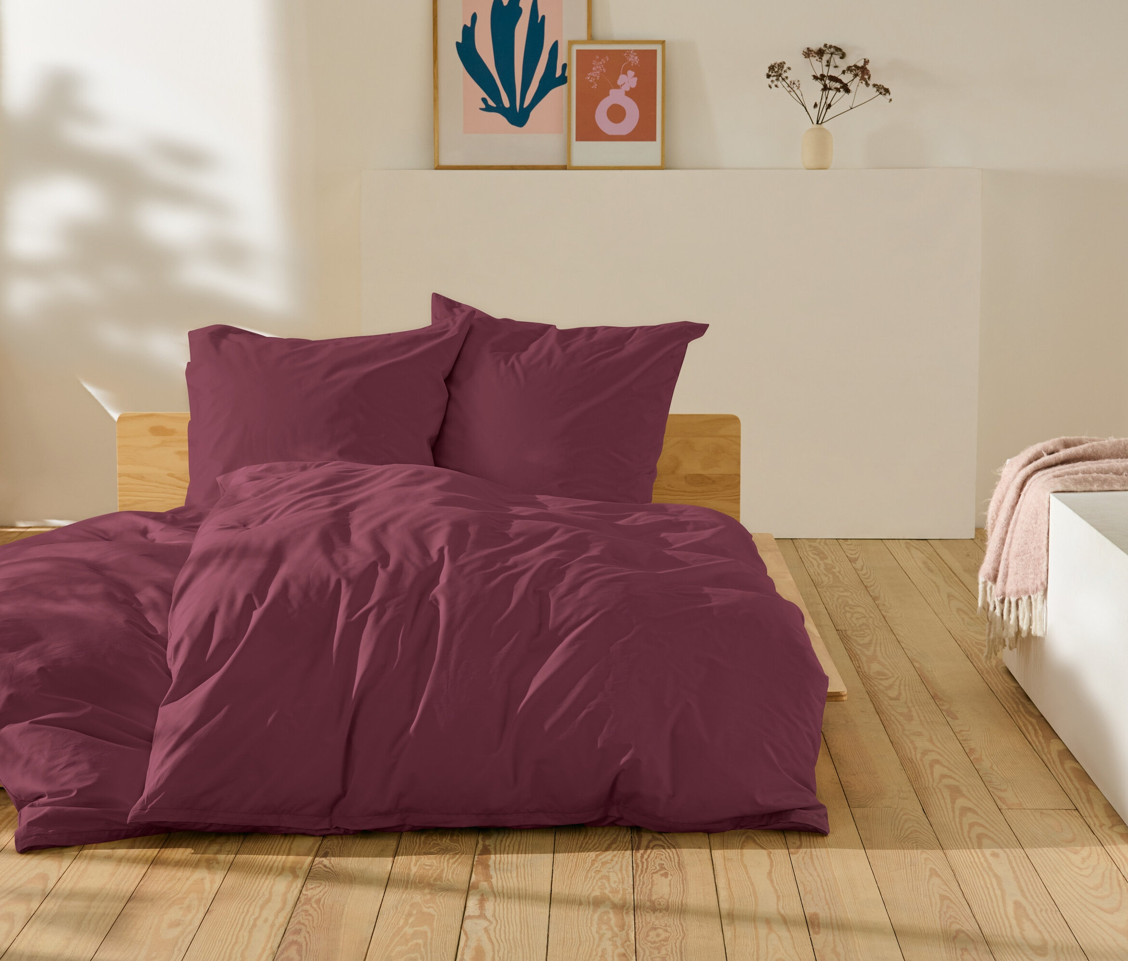 Vínové ložní prádlo leží na posteli na dřevěné podlaze.