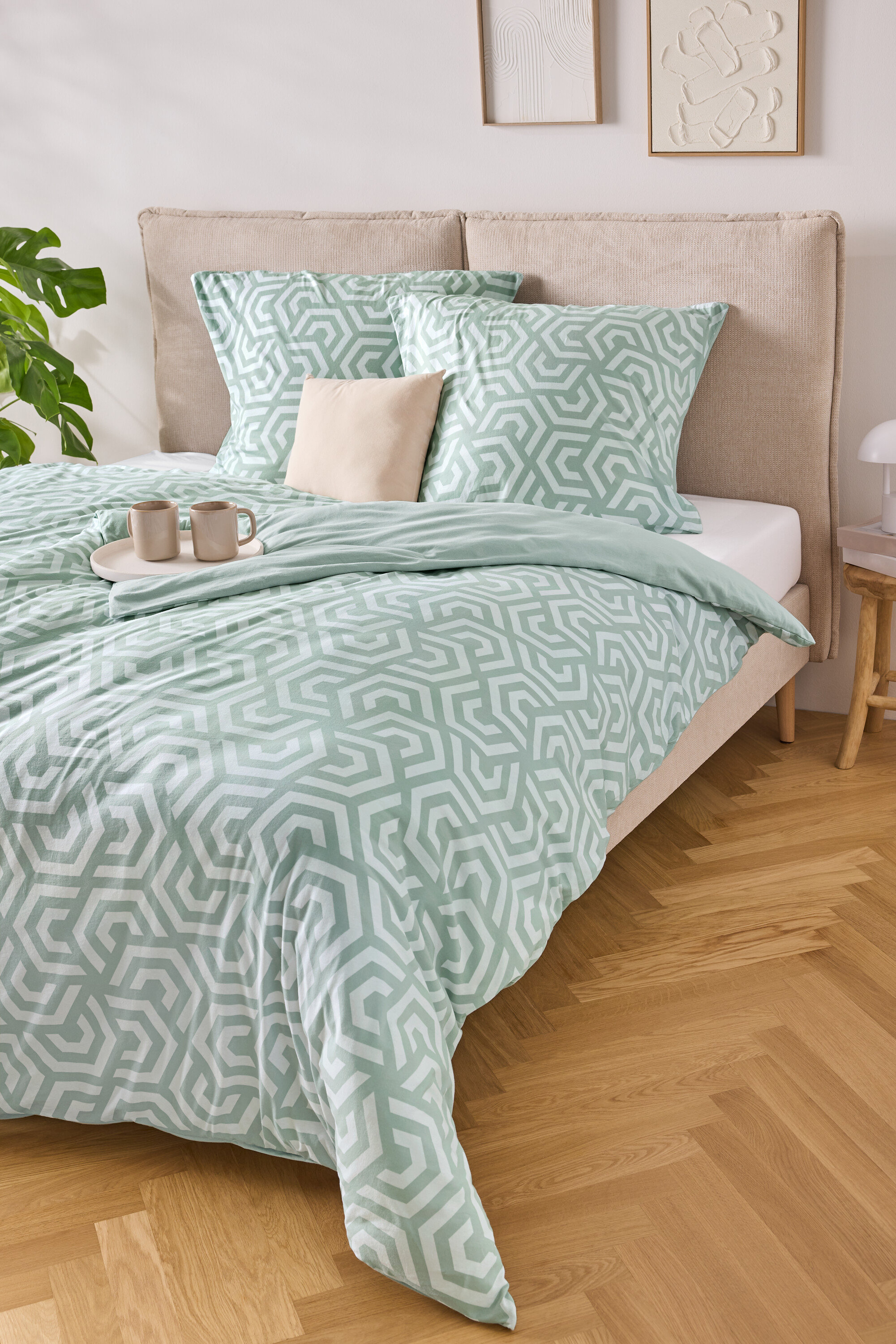 Postel se světle modro-bílým pruhovaným ložním prádlem, dvěma polštáři a podnosem se dvěma šálky.