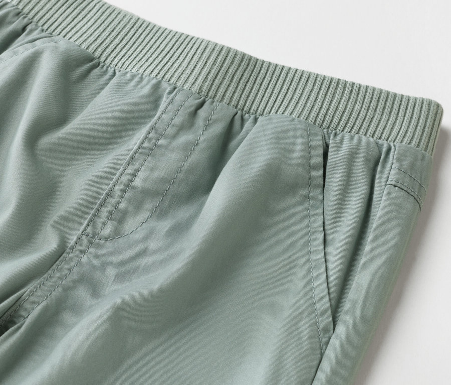 Detailní záběr světle zelených kalhot s elastickým pasem.