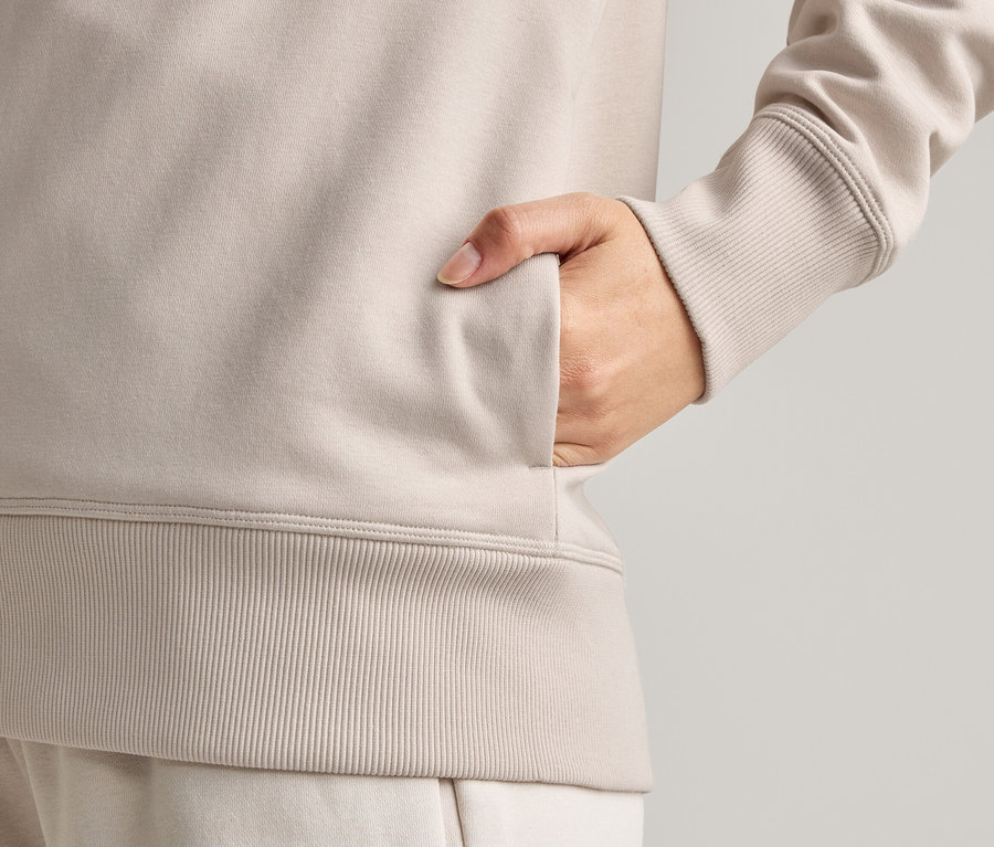 Detailní záběr osoby, která si dává ruku do kapsy světle hnědé bundy.