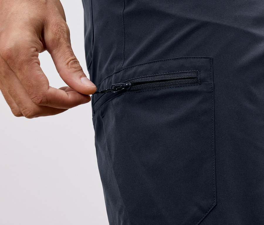 Detailní záběr ruky zapínající zip na tmavě modrých kalhotách.