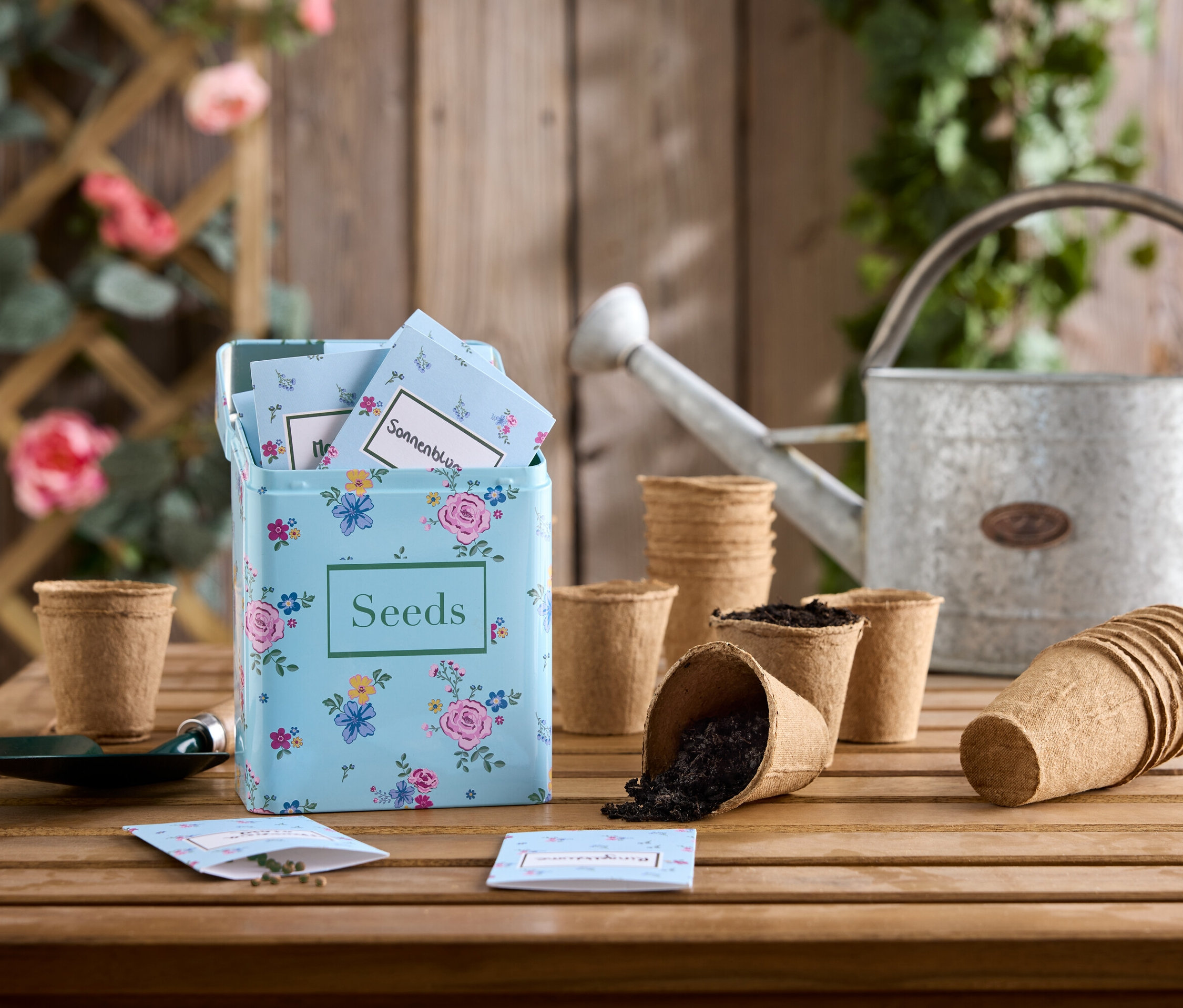 Sada květinových semen na dřevěném stole s pozinkovanou konví a sadbovači.