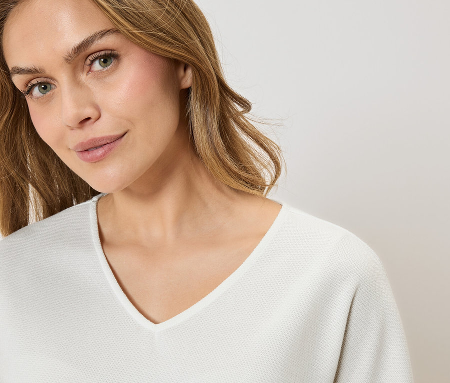 Portrét ženy s blond vlasy v bílém svetru s výstřihem do V.