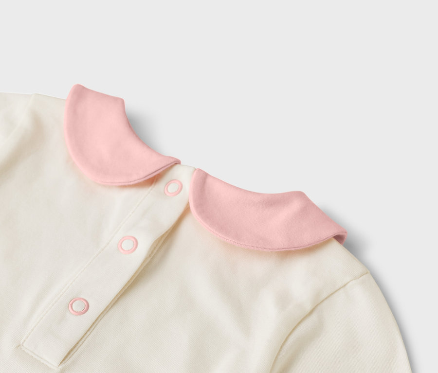 Detailní pohled na krémový top s růžovým límcem a knoflíky.