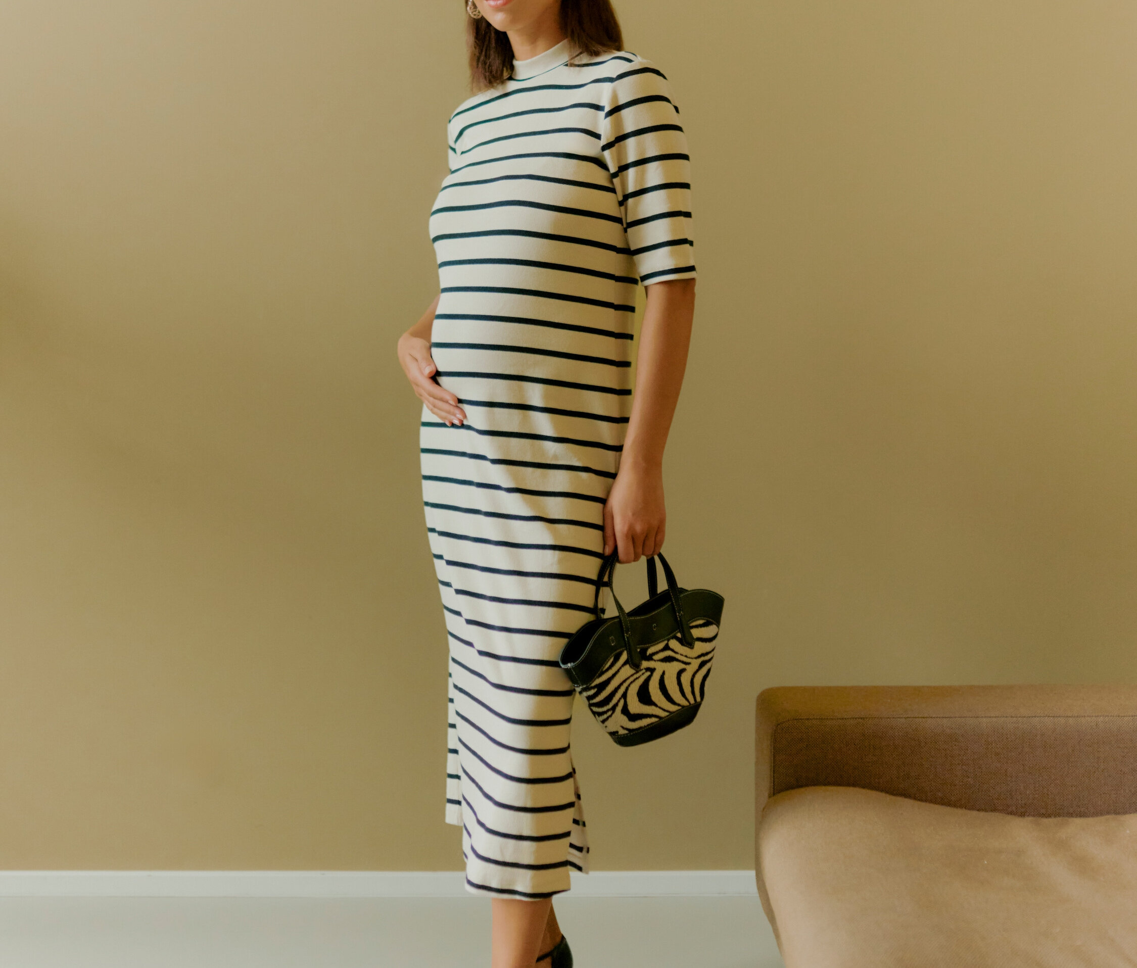 Žena stojí a drží zebra kabelku. Má na sobě pruhované šaty a černé boty.