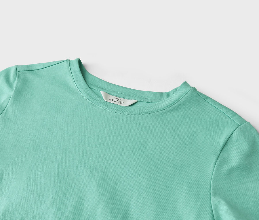 Detailní záběr světle tyrkysového trička s etiketou s nápisem "TCHIBO MY STYLE".