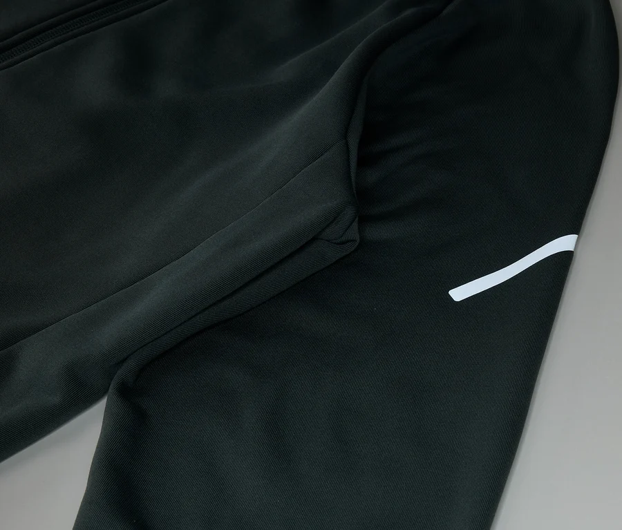 Detail černých tepláků s kapsou na zip a bílým pruhem.