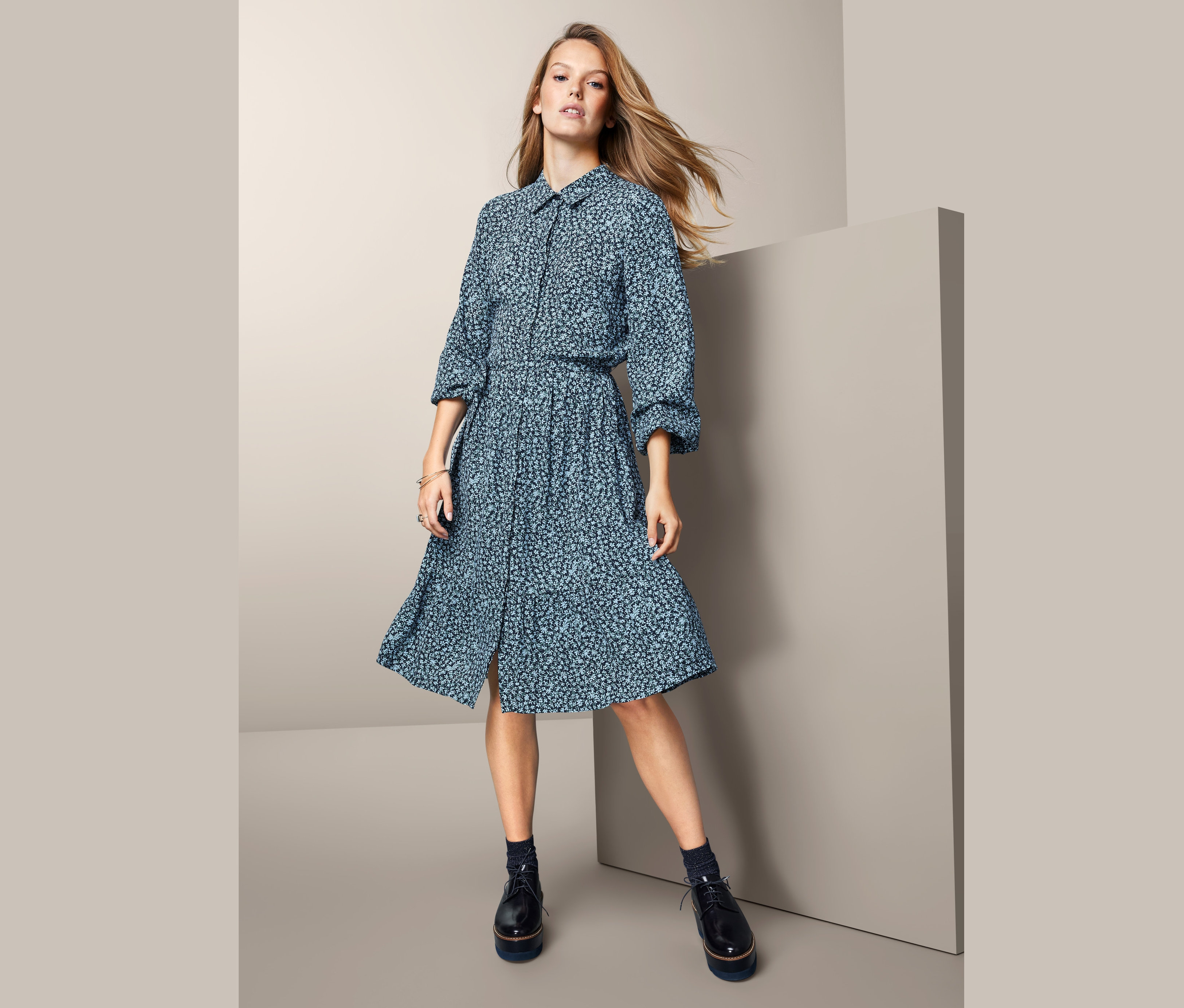 Žena stojí a má na sobě květované halenkové šaty.