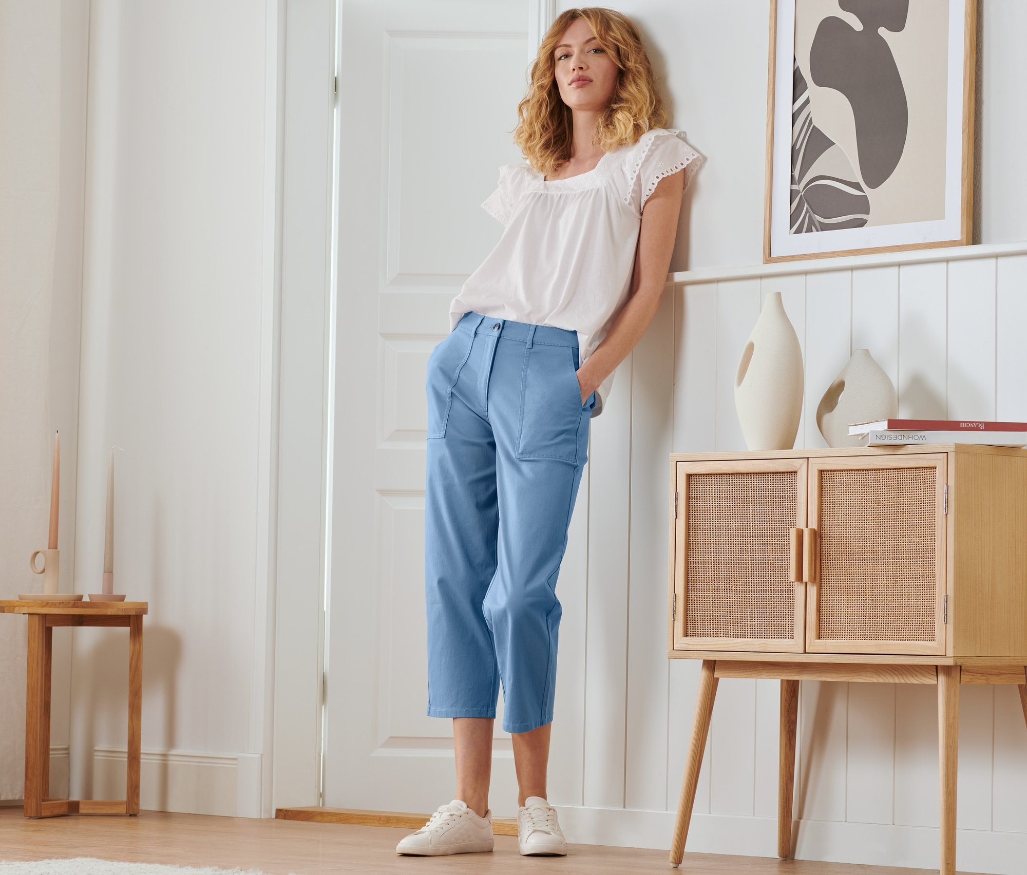 Žena pózuje v letních kalhotách chino a bílé halence.