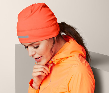 Žena v oranžové bundě a termo čepici se sklání k zemi.