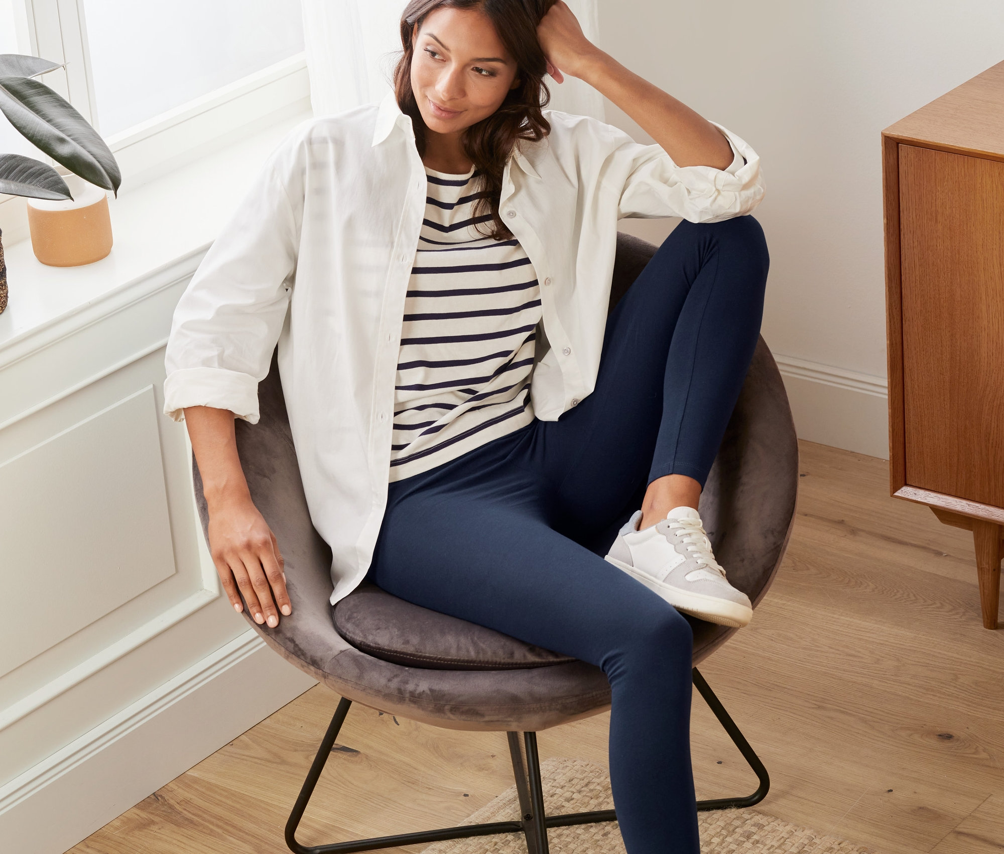 Žena sedí v křesle a má na sobě tmavě modré legíny.