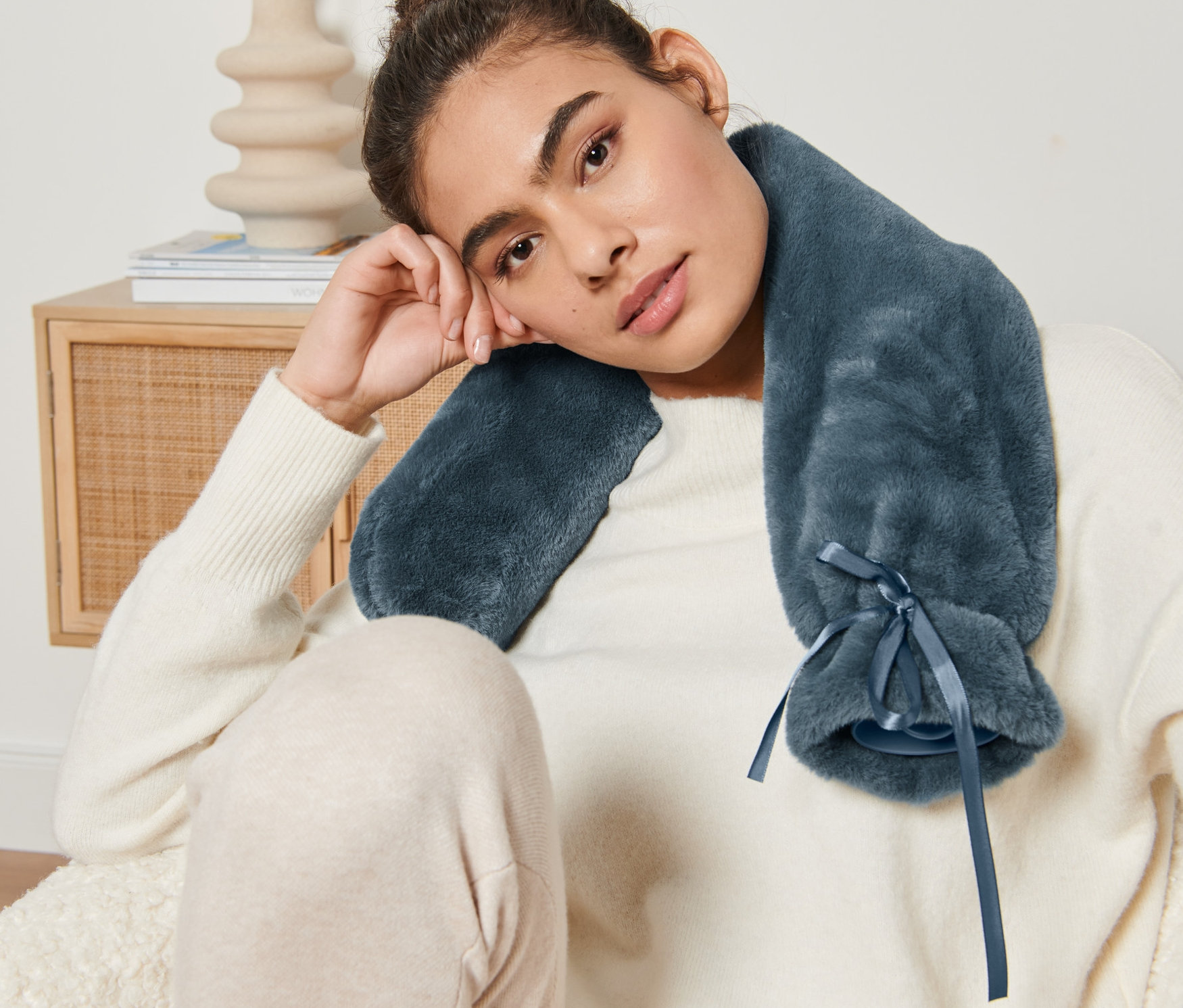 Žena sedí a má na krku dlouhý modrý termofor.