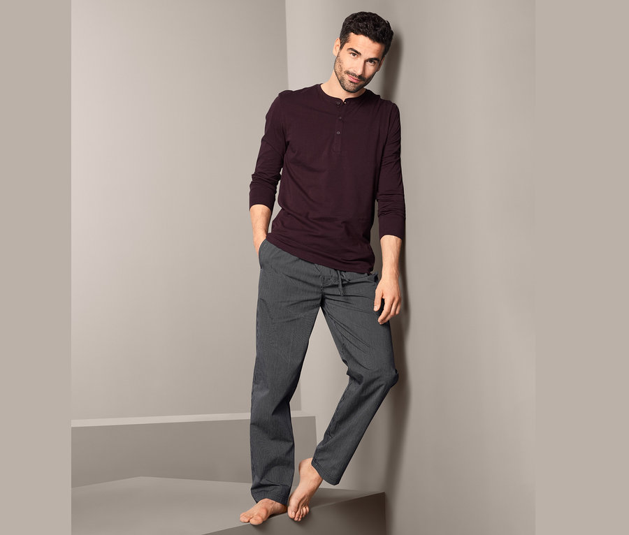 Muž opřený o zeď má na sobě pyžamo.