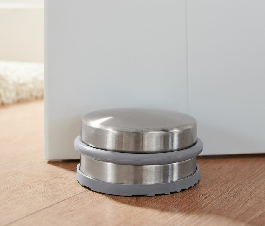 Kovová zarážka dveří na dřevěné podlaze u bílých dveří.