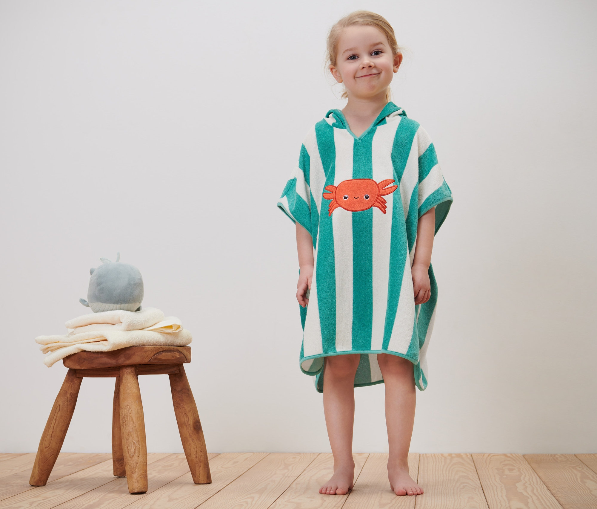 Holčička stojí a má na sobě froté pončo pro miminka a pro děti se vzorem kraba.