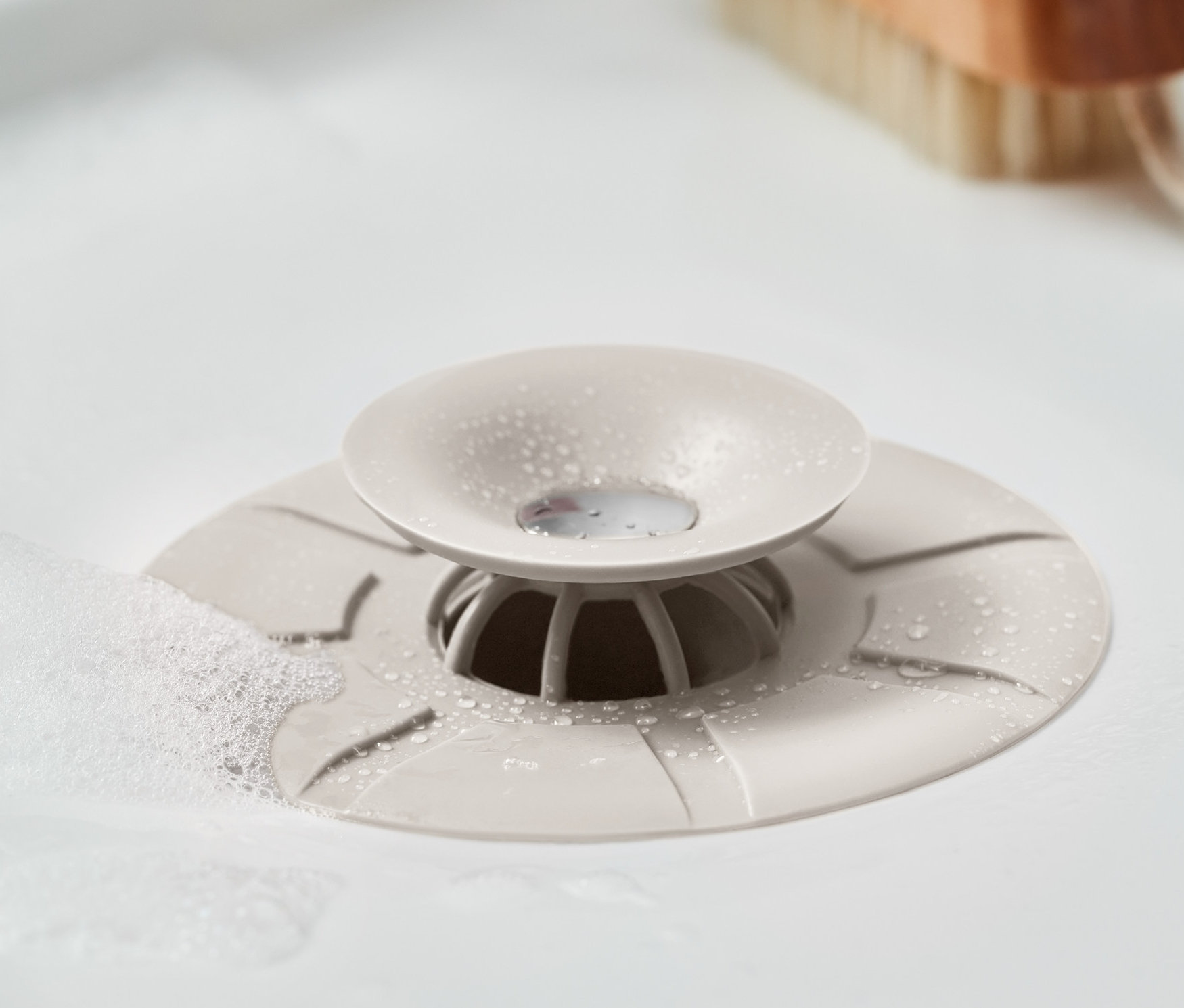 Detailní záběr odtokového sítka a zátky v umyvadle s bublinkami.