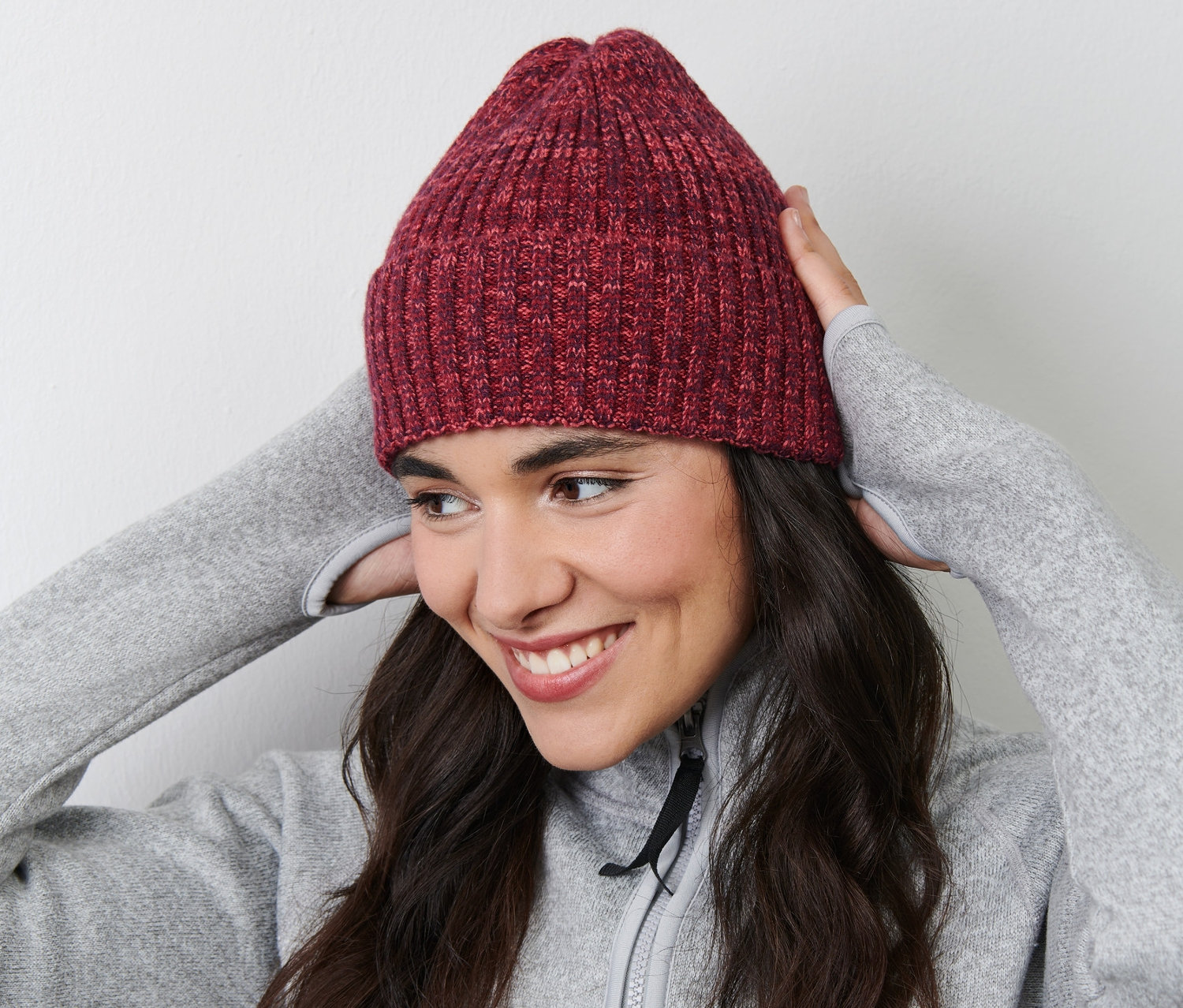 Žena se usmívá a upravuje si pletenou čepici na hlavě.