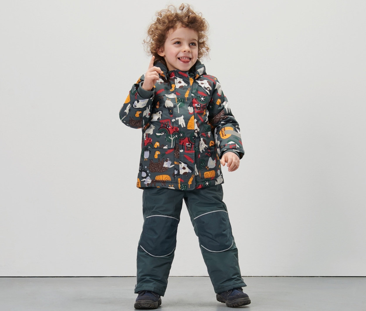 Chlapec stojí a má na sobě dvoudílnou kombinézu do sněhu s celopotiskem statku.