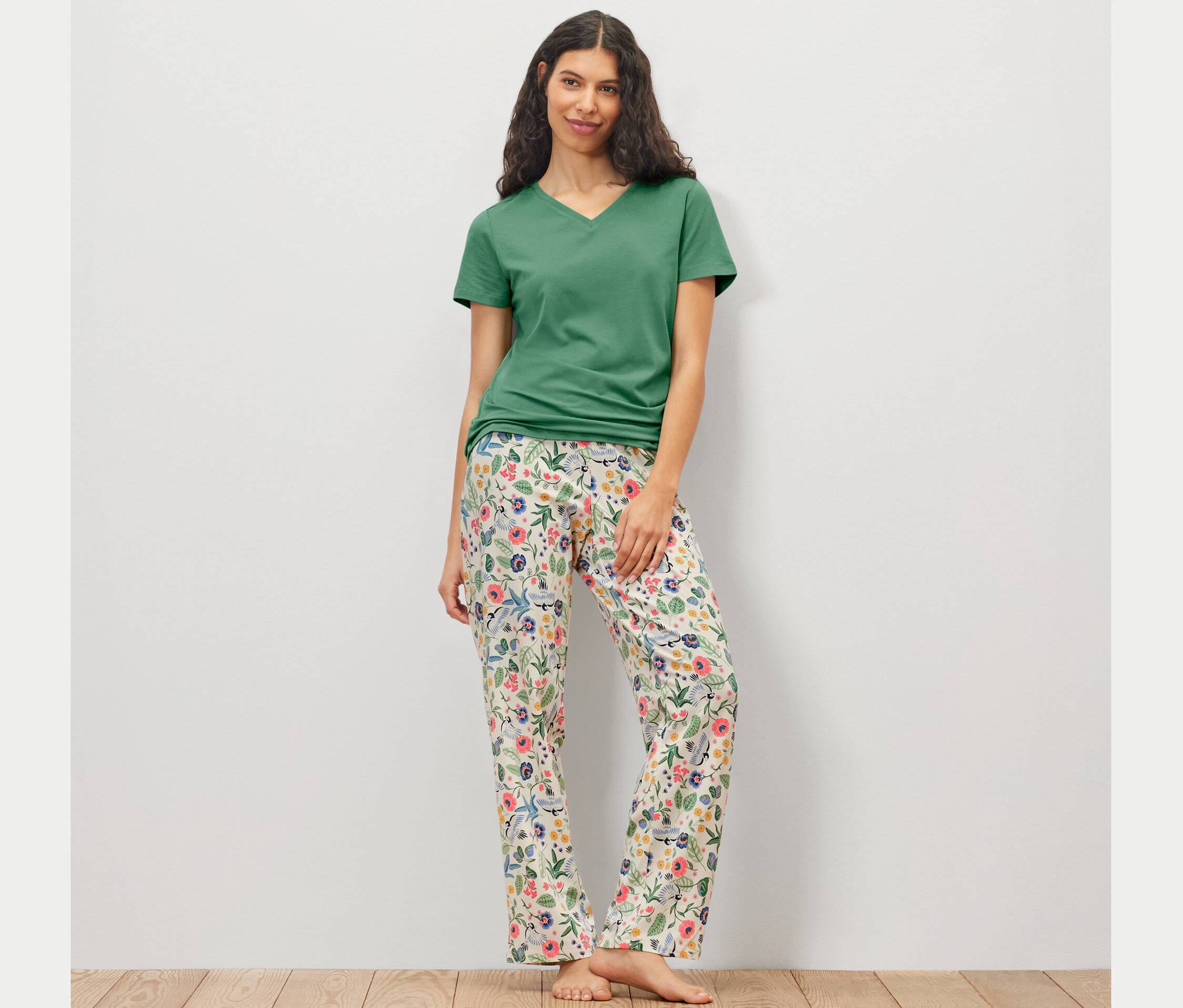 Žena v pyžamové soupravě s květinovými kalhotami a zeleným tričkem.