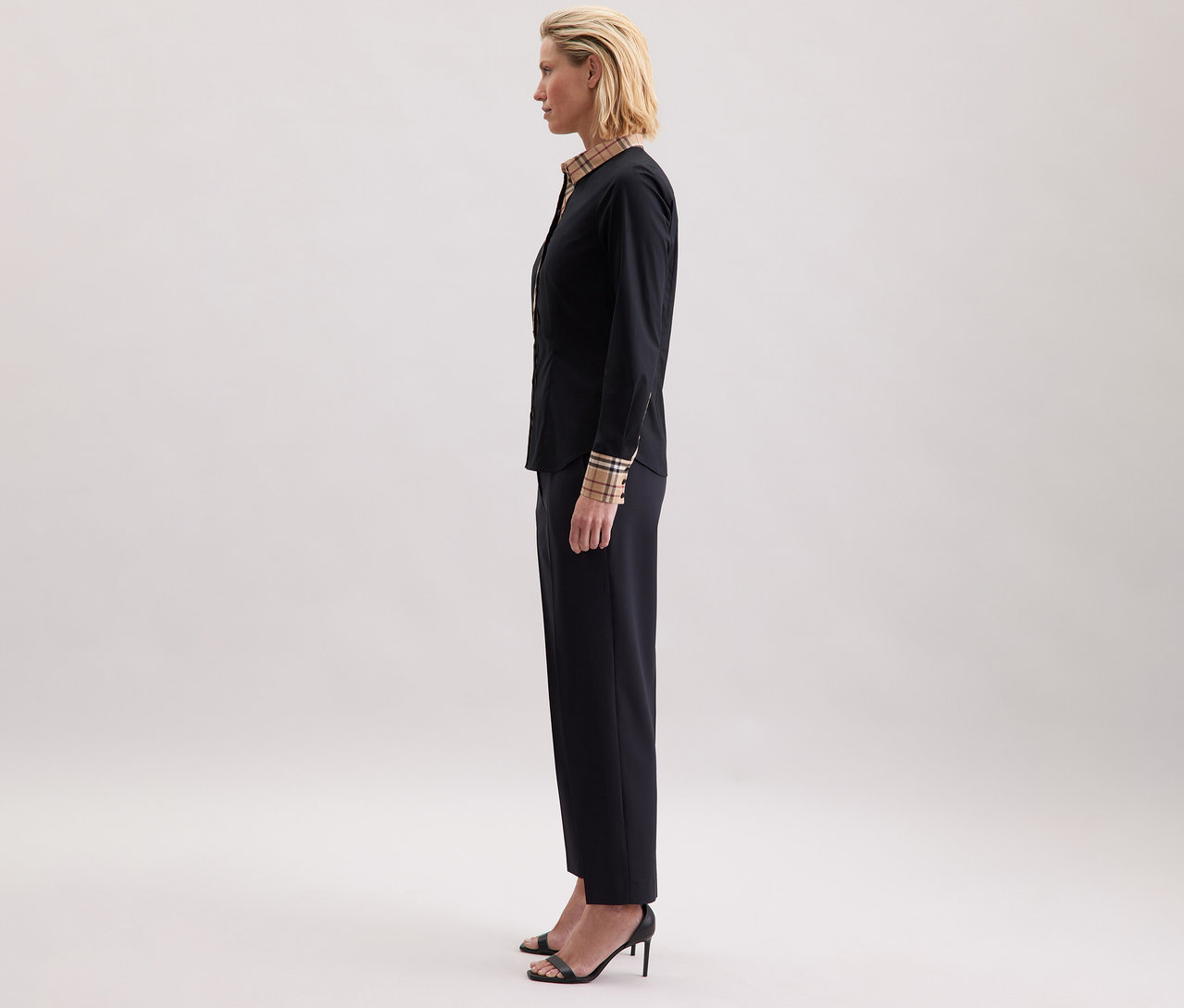 Žena z profilu má na sobě popelínovou halenku Seidensticker s kostkovaným detailem, tmavé kalhoty a sandály na podpatku.