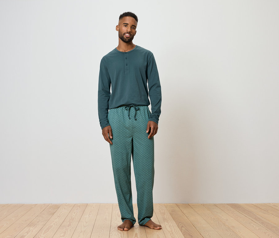 Muž stojí a má na sobě zelené pyžamo.