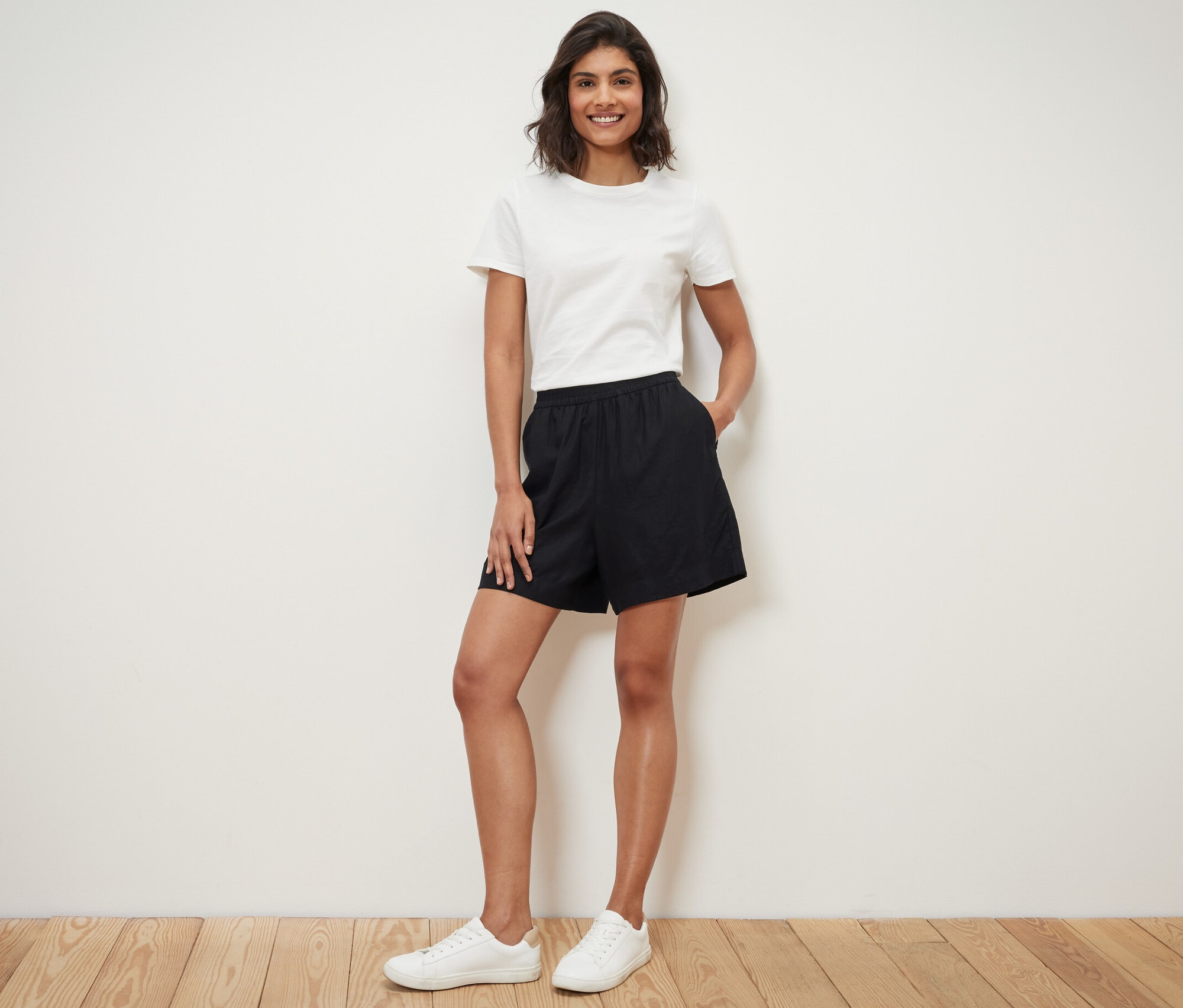 Žena stojí a má ruce v kapsách černých lněných šortek.