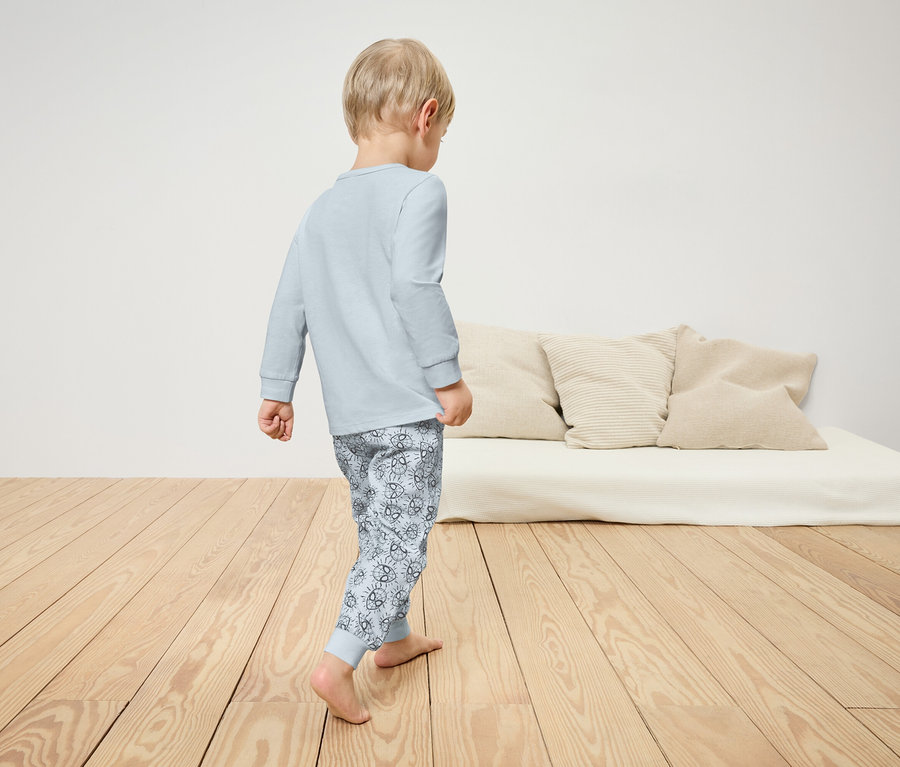 Chlapec v pyžamu kráčí po dřevěné podlaze. Na pozadí je vidět postel s polštáři.