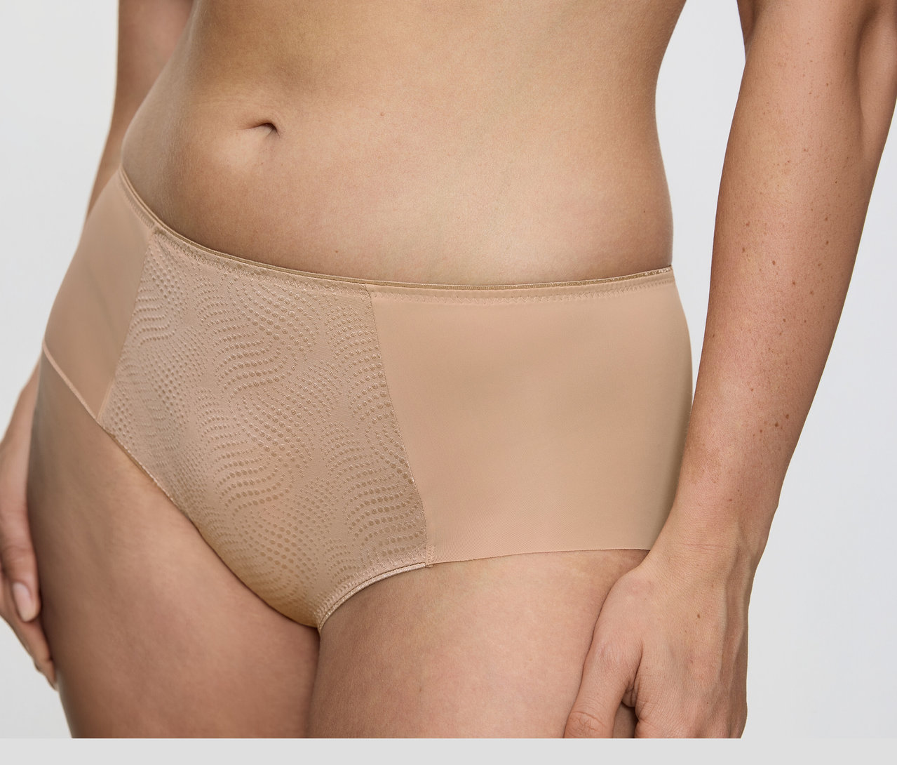 Detail trupu osoby v tělových zmenšujících bokových kalhotkách Triumph Essential »Minimizer Hipster X« s hladkou látkou po stranách a texturovaným, vzorovaným síťovaným panelem vpředu.