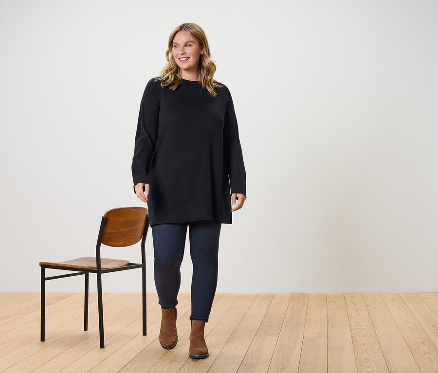 Žena kráčí a má na sobě dlouhý pletený svetr tmavě hnědé barvy a legíny v džínovém vzhledu s podšívkou.