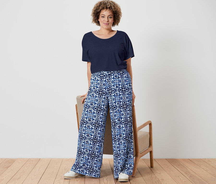 Žena pózuje v námořnicky modrém tričku ze směsi lnu a modrých kalhotách se širokými nohavicemi s potiskem.